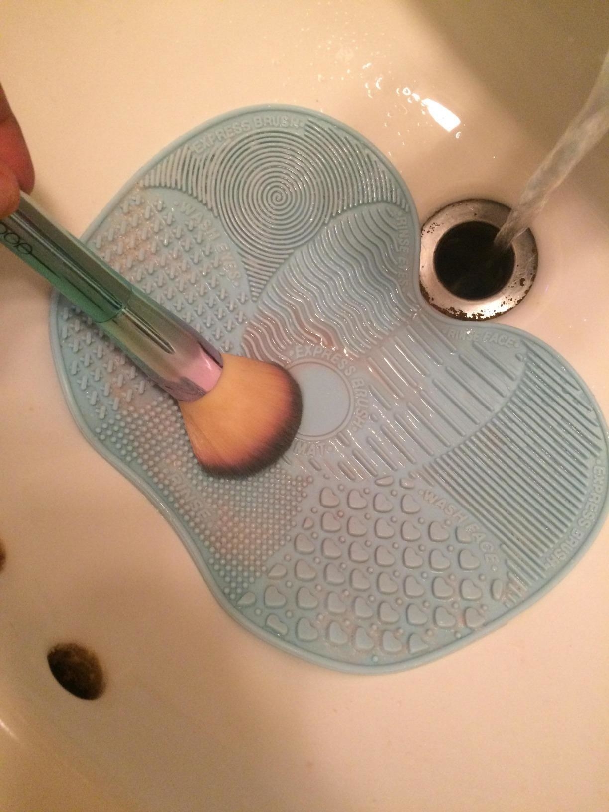 A reviewer washing a brush on the mat, which is suctioned onto her sink
