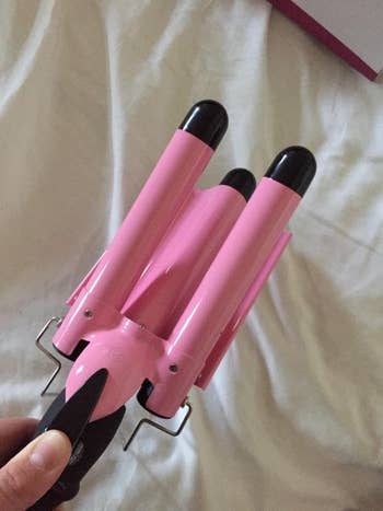Hand holding the pink three-barrel curling iron 