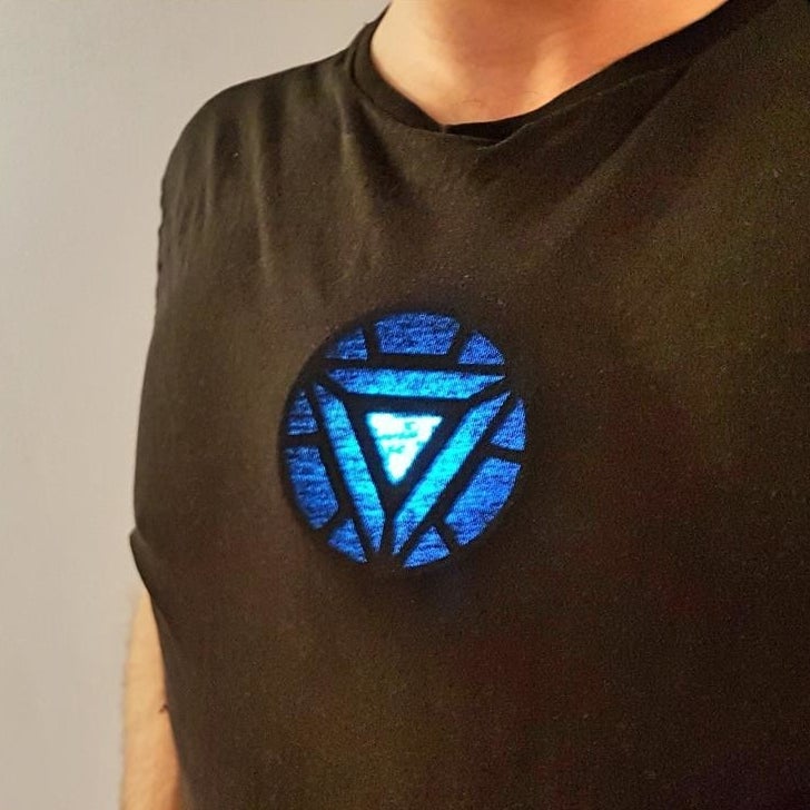 A person wearing a glowing arc reactor replica under their shirt