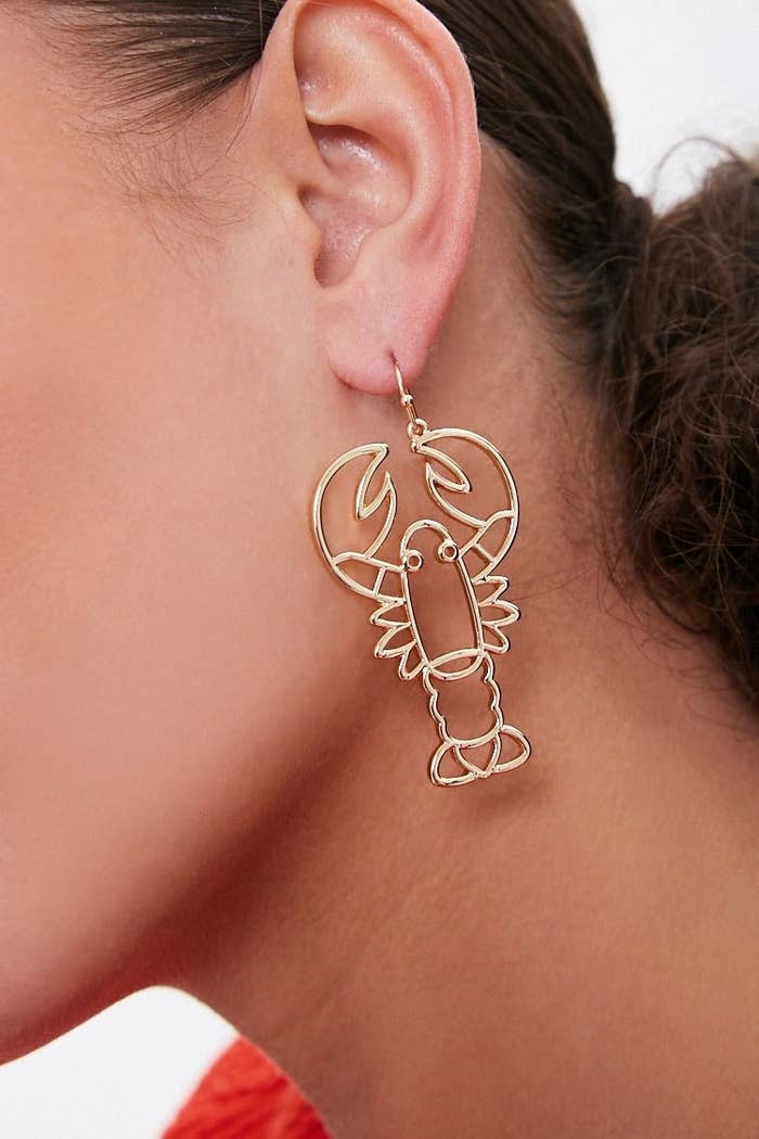Model wearing gold earrings in the shape of a lobster
