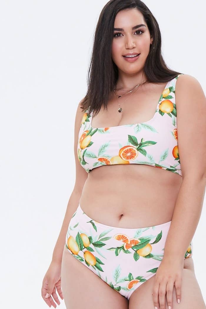 Model wearing square-neck bikini top and bottom in pink with a print of oranges and leaves on it