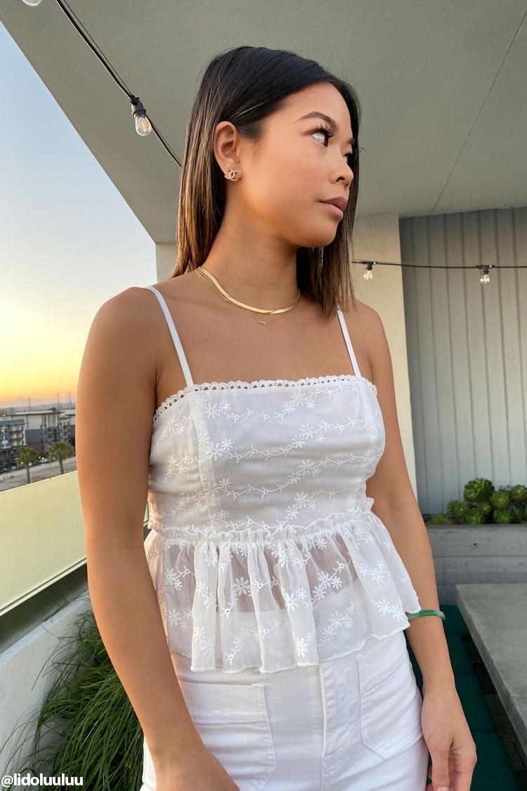 Model wearing cami with ruffled trip, straight neckline, and adjustable straps in white