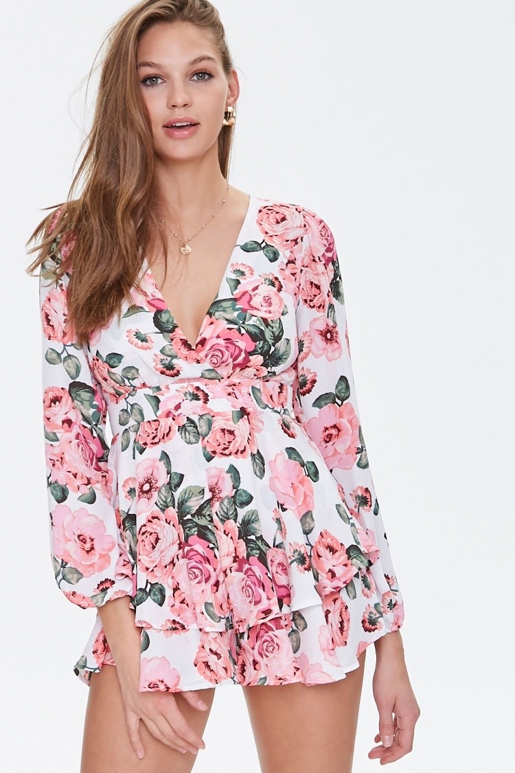 A model wearing the deep V-neck, long sleeved romper with a white background and pink and green flowers