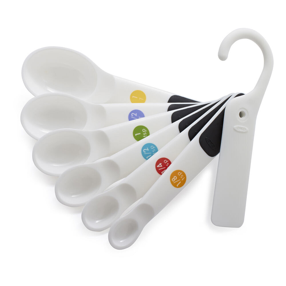 a set of seven white measuring spoons in different sizes with different colored circles on each one to indicate the measurement