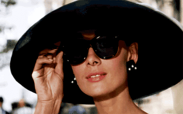 Audrey Hepburn lowering her sunglasses with a big hat on her head 