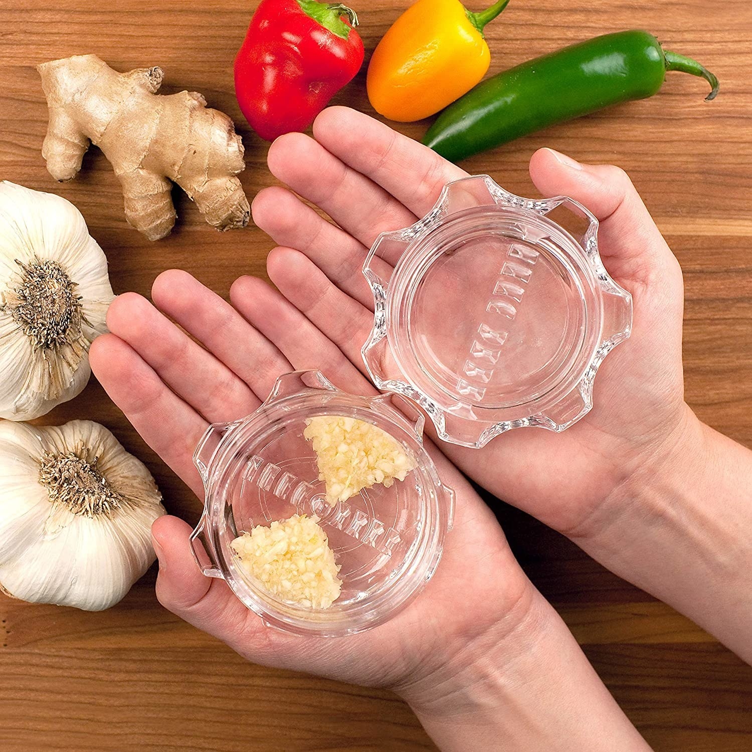A pair of hands holding the garlic twist, which is made up of two transparent gear-shaped pieces with rows of teeth inside 