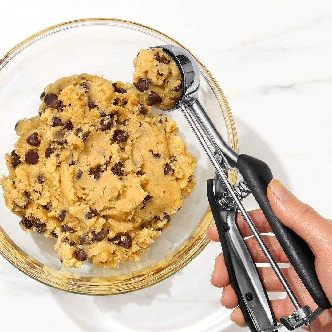 a model holding the cookie scoop while scooping up a measured amount of cookie dough from a bowl