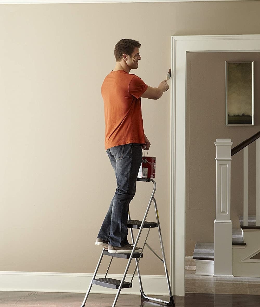 Model using the step stool to paint a high-up area of a wall 