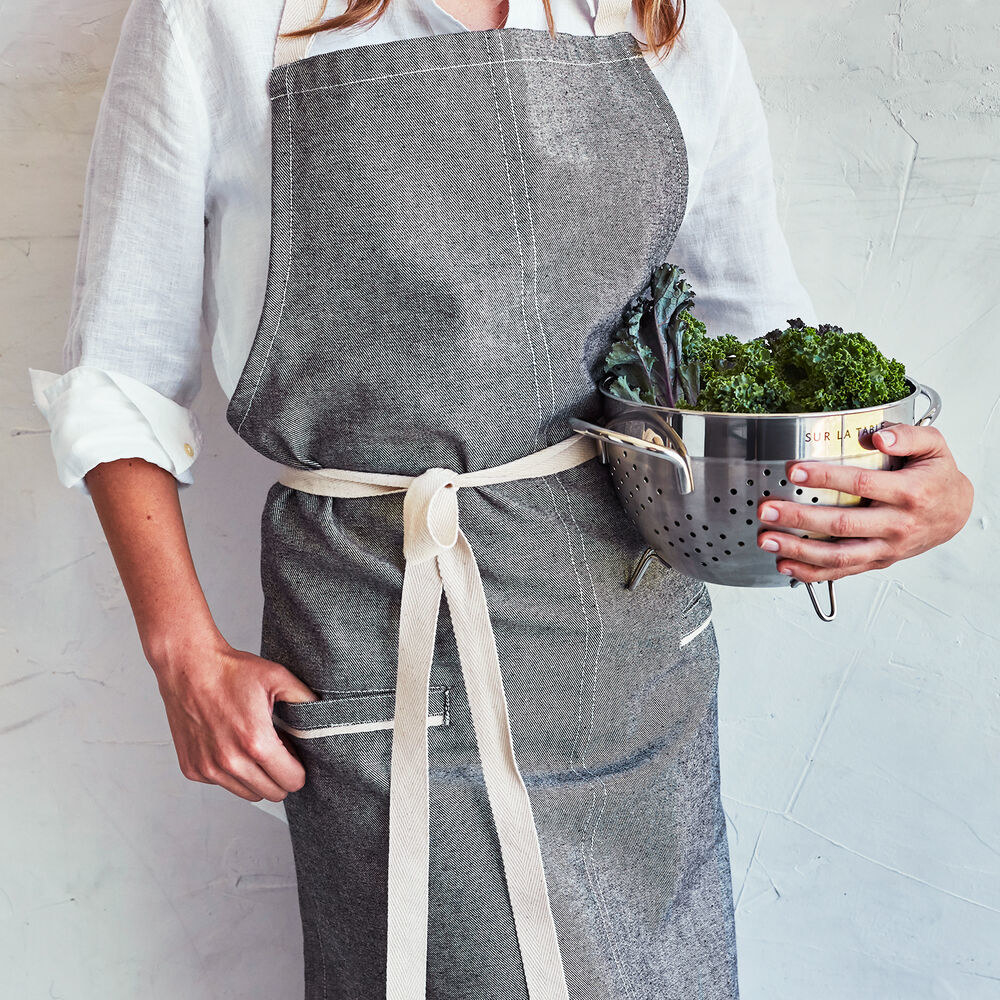 a gray apron made of raw denim with off-white accents on the straps and pockets