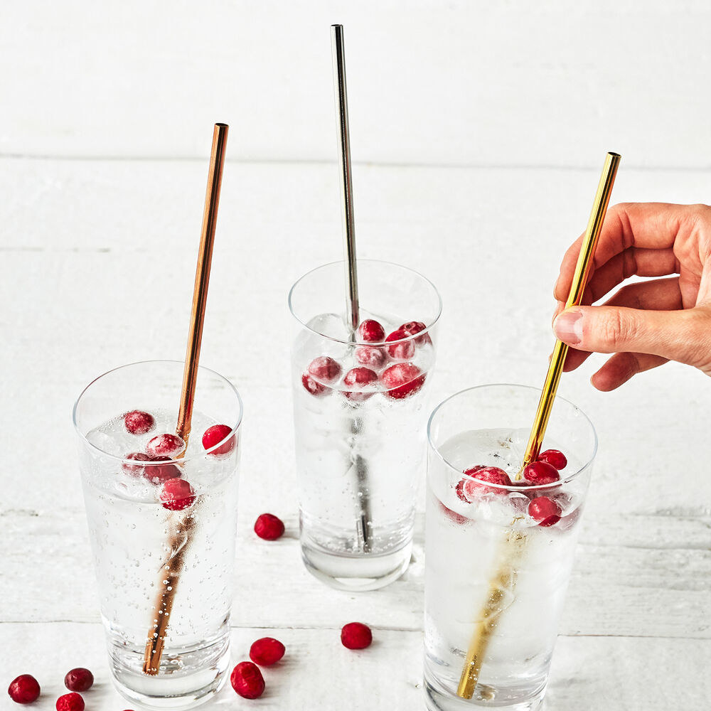 a single copper straw, silver straw, and gold straw placed in three indivudal glasses of water with cranberries in it