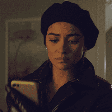 Gif: Shay Mitchell rolls her eyes hard, sighing, before she looks back at her phone