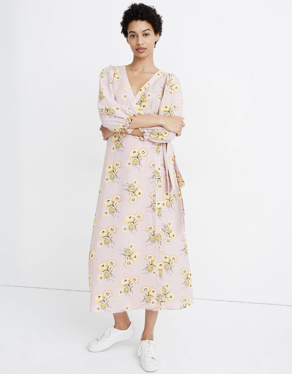A model in a pale purple flowery wrap dress with 3/4 sleeves that falls above the ankle 