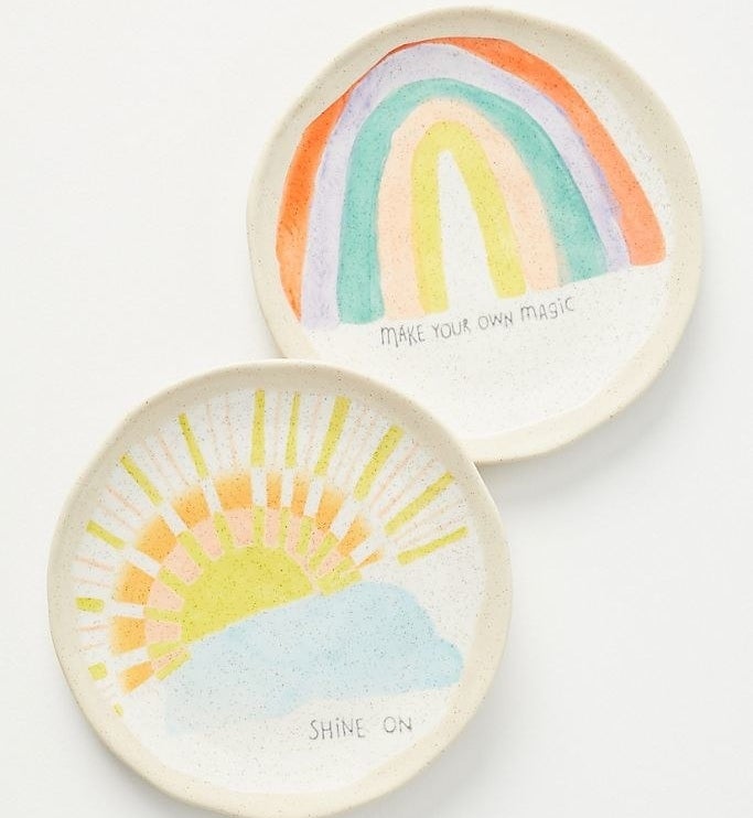 A plate with a watercolor painted sun coming out of a cloud that says &quot;Shine On,&quot; and another play with a painted rainbow that says &quot;Make Your Own Magic&quot; 