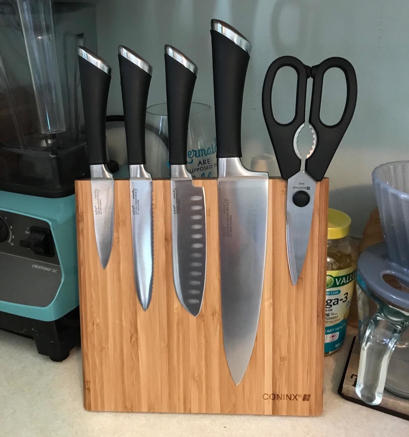 review image of thin wooden board with four knives and a pair of scissors stuck to it 