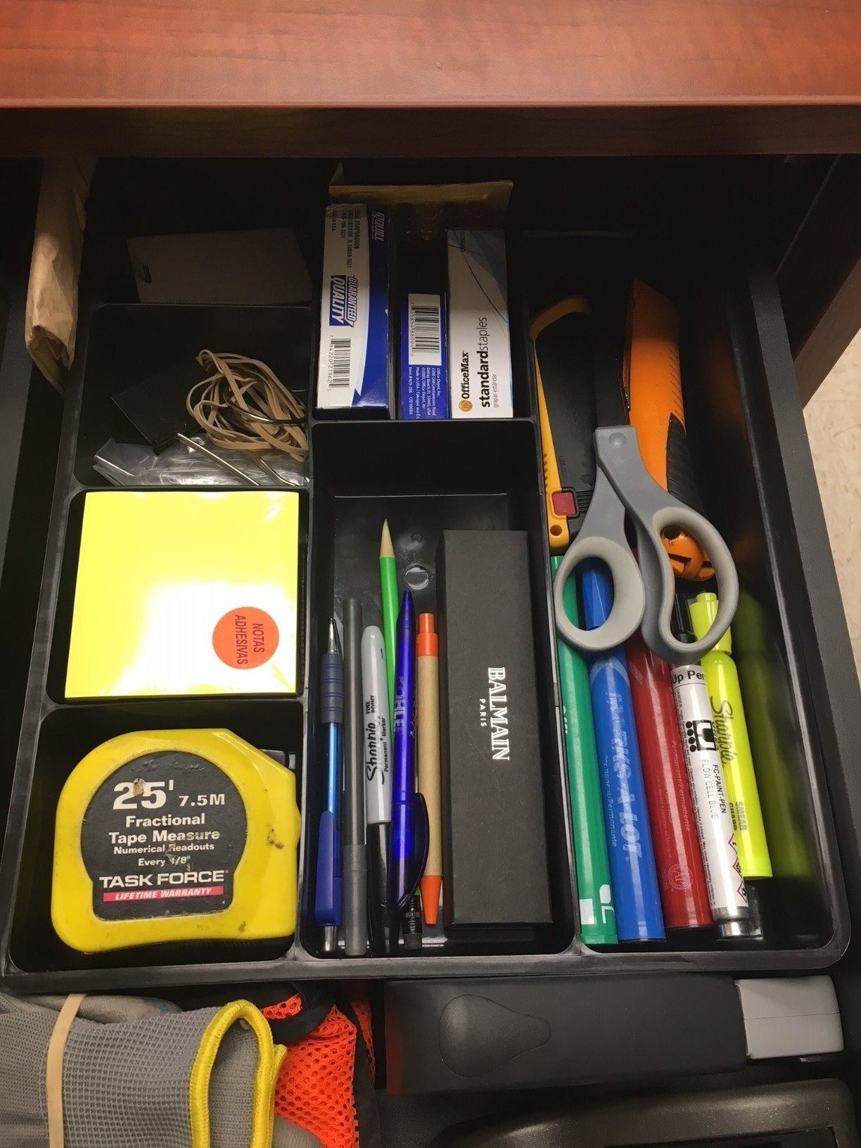 Reviewer photo of a drawer insert with seven differently-sized compartments with assorted office supplies in them
