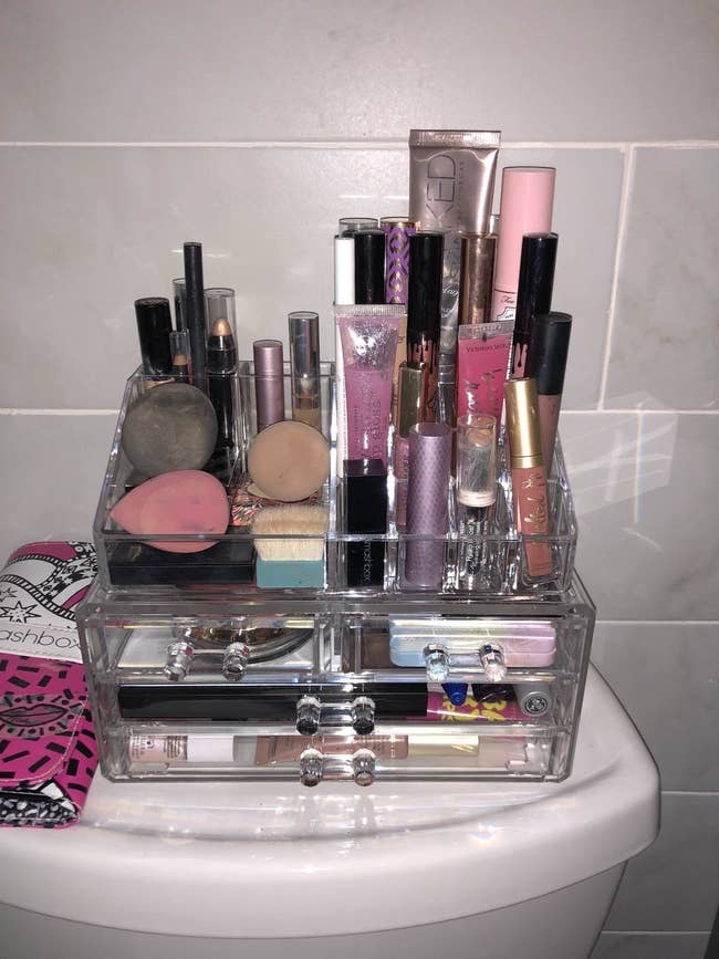 reviewer image of the clear storage box with two long drawers, two half drawers and an upright storage area on top filled with all different kinds of makeup
