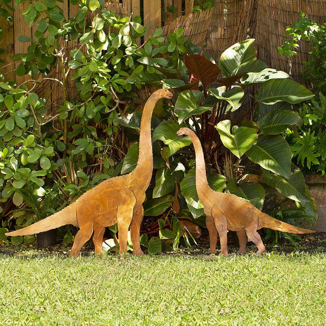 small brontosaurus shaped yard decorations in front of a bush