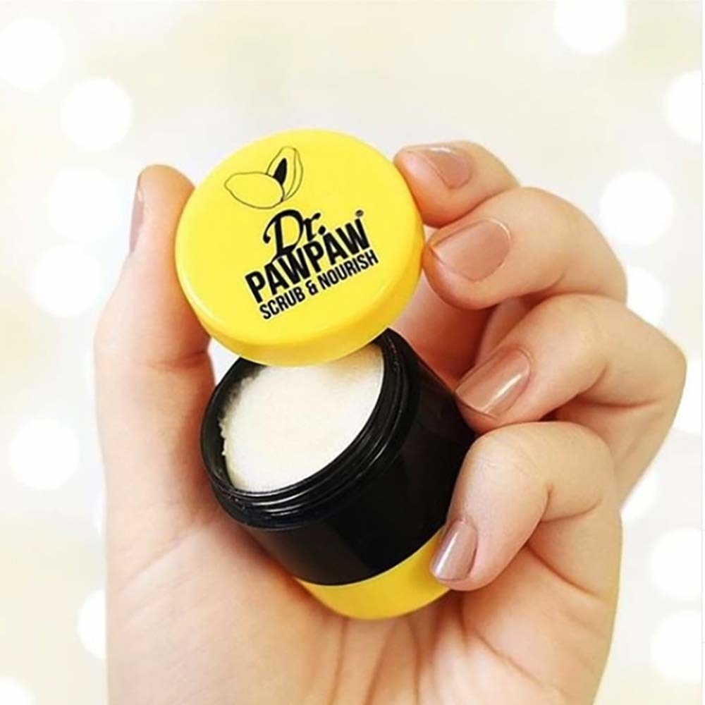 hand holding yellow and black palm-sized tub with the cap labeled &quot;Dr. Pawpaw scrub &amp;amp; nourish&quot; while the jar contains white, gritty product 