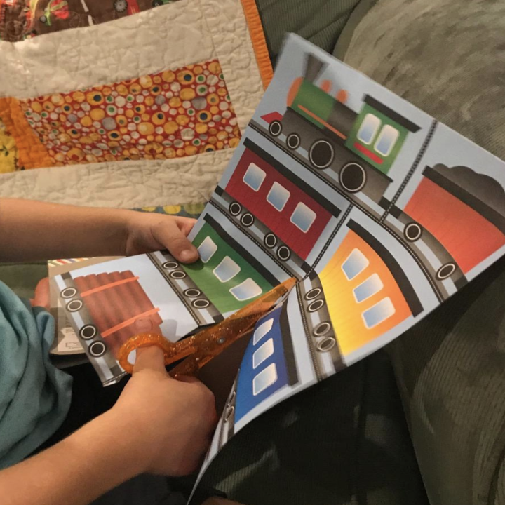 A child's hand cutting a page of trains with the scissors