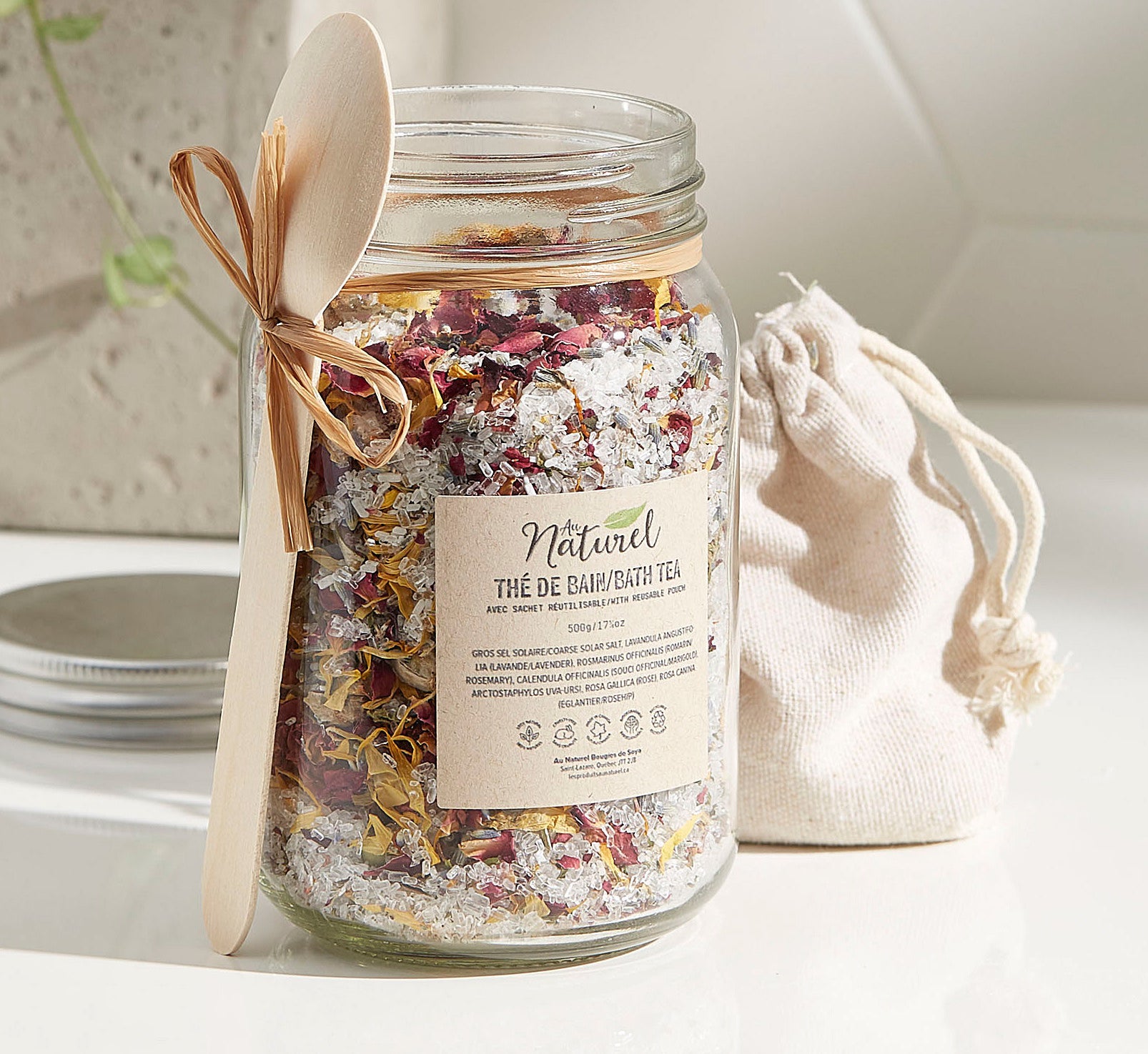 A large jar filled with bath salts There is a small wooden spoon tied around the jar with a string