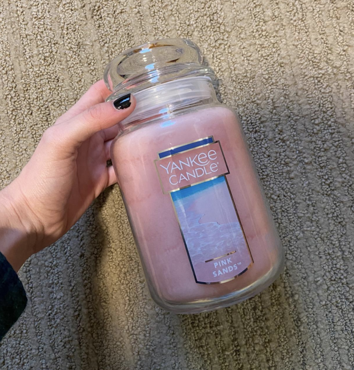 A reviewer&#x27;s hand holding the biggest jar of the &quot;Pink Sands&quot; Yankee Candle