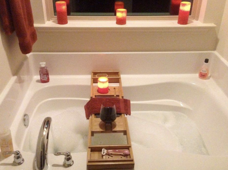 the tray spread across the bath tub with a book, a razor, and a glass of wine on it