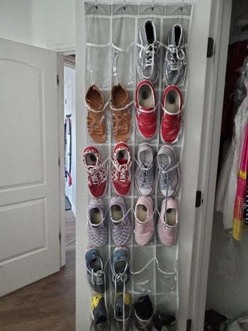 a reviewer photo of the vinyl shoes organizer hanging on a door with shoes in the pockets 