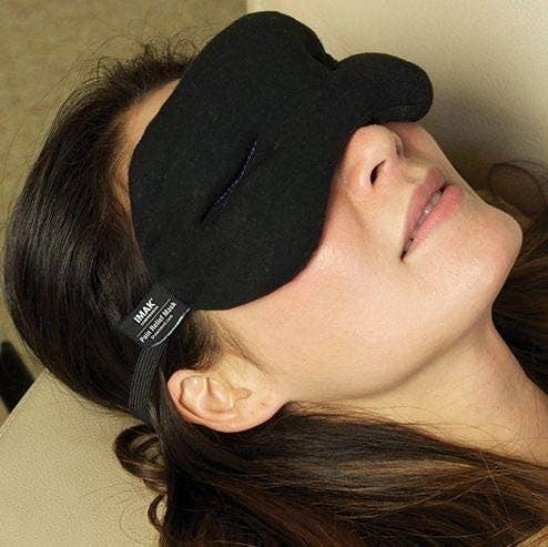 person's head resting on the arm of a chair while they wear the eye mask