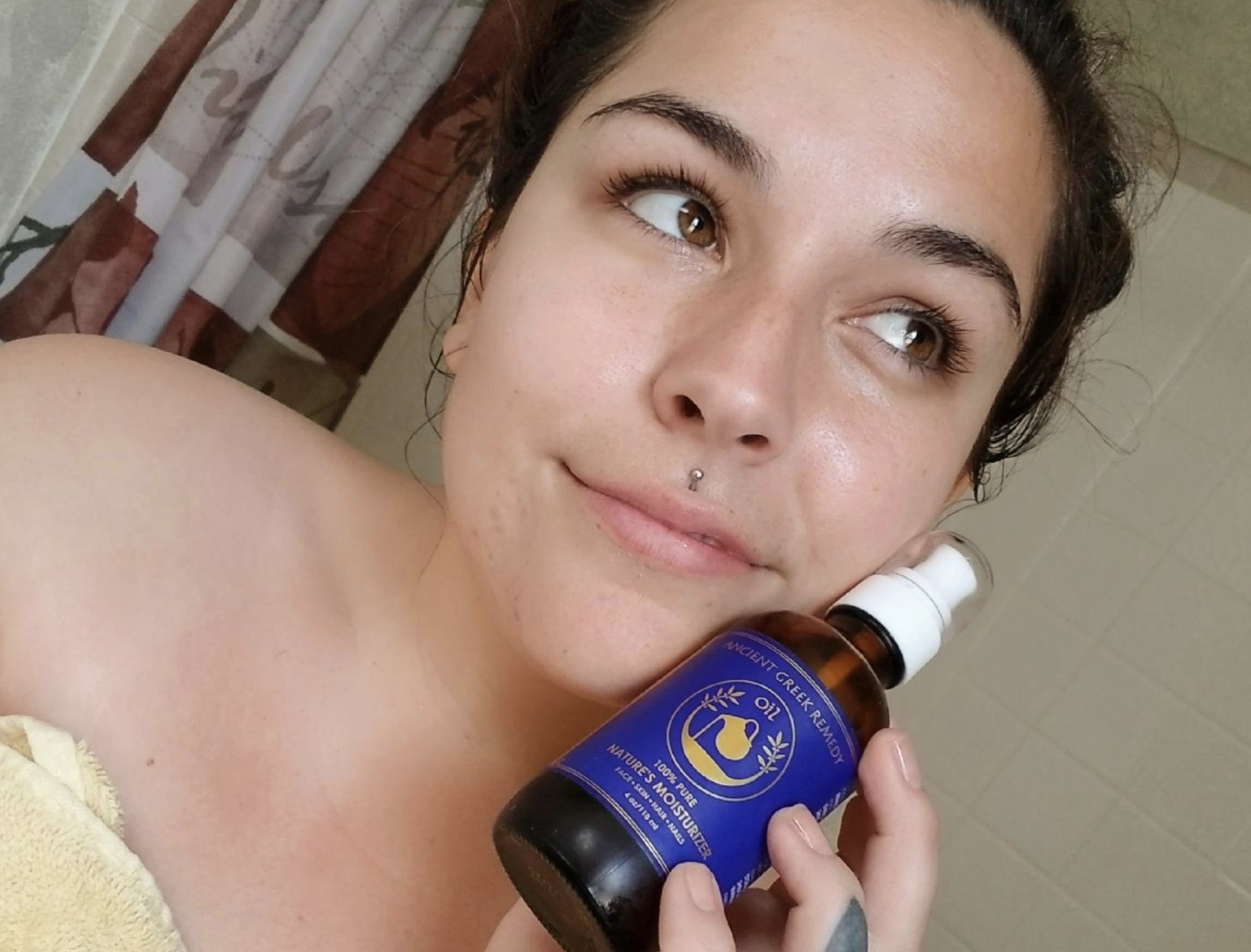 A reviewer holding the spray bottle of oil next to their face