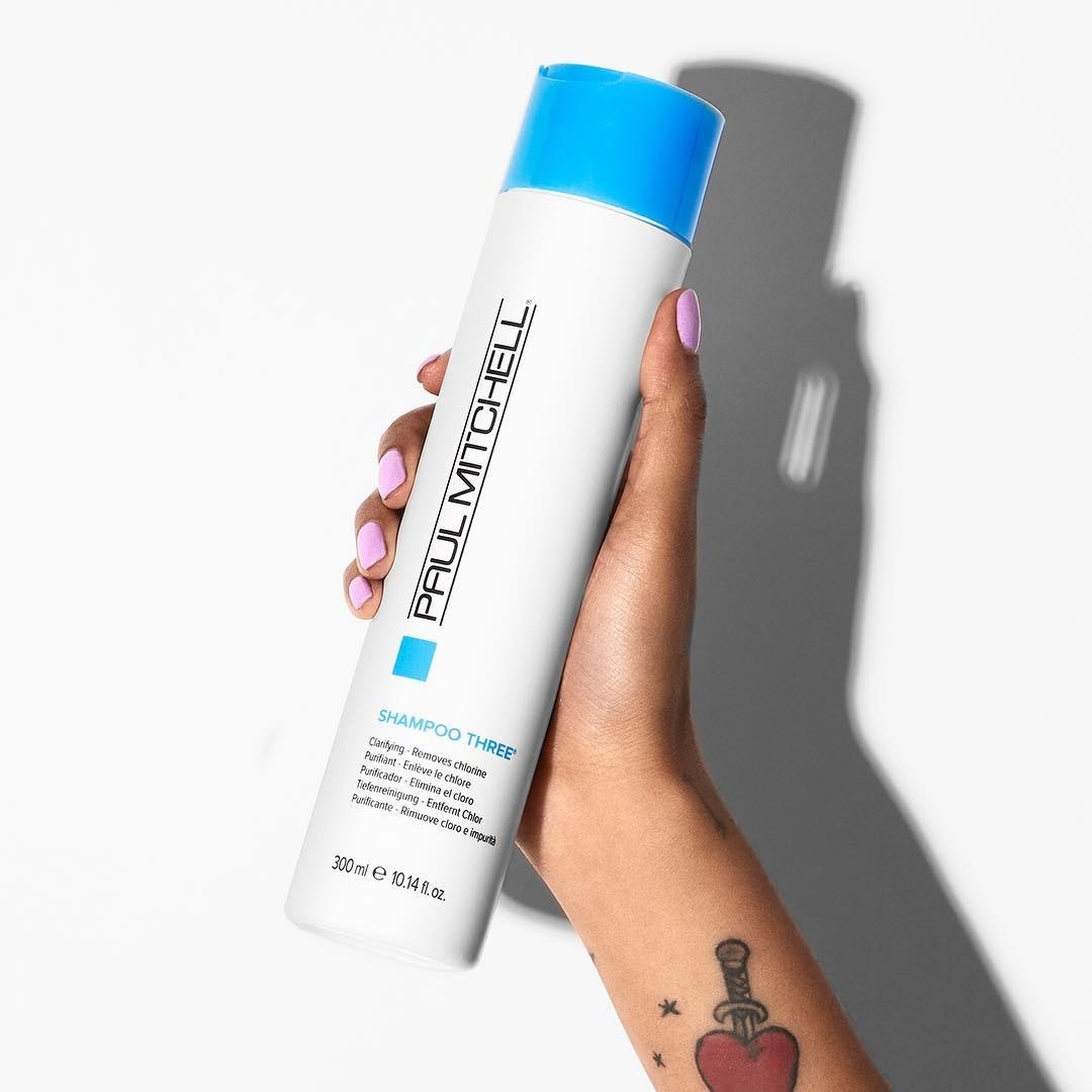 hand holding white bottle with blue cap labeled "Paul Mitchell"