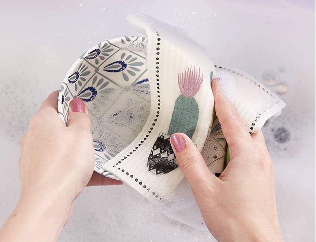 Close up of a model's hands using the dishcloth with a cacti design and dotted boarder to clean a bowl