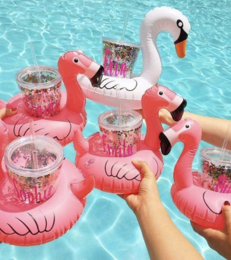 A group of reviewers poses with pink flamingo drink floaters in a pool