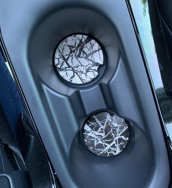 Reviewer's picture of the black and white marble car coasters in the cup holders in their car.