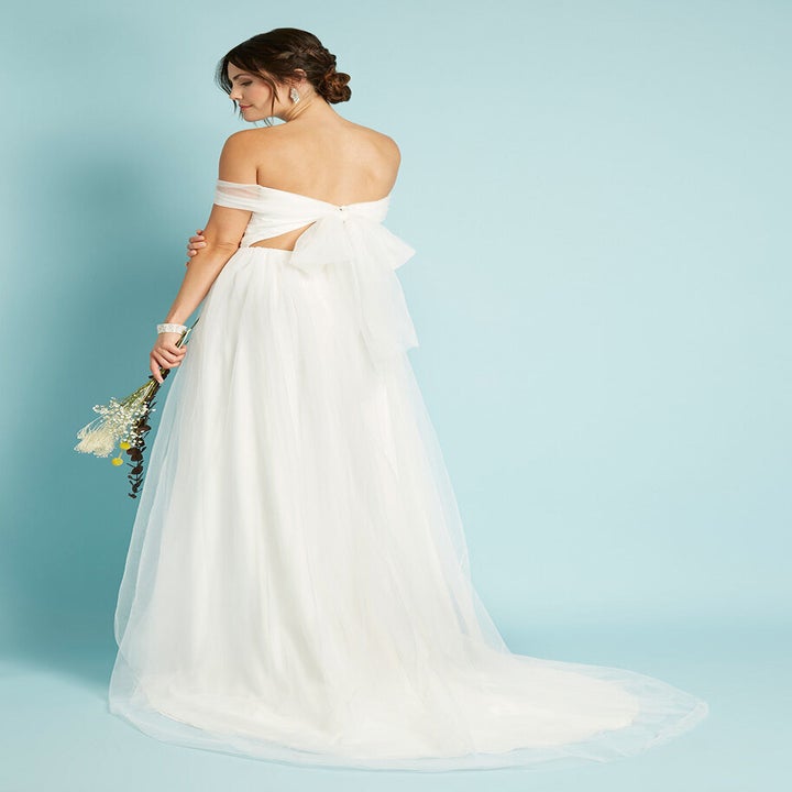 a model showing the back of a floor length tulle gown with a cut out in the lower back area and a beautiful big bow