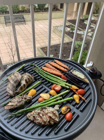 Another reviewer's photo of the portable grill heating up meat, asparagus, and other veggies on a balcony