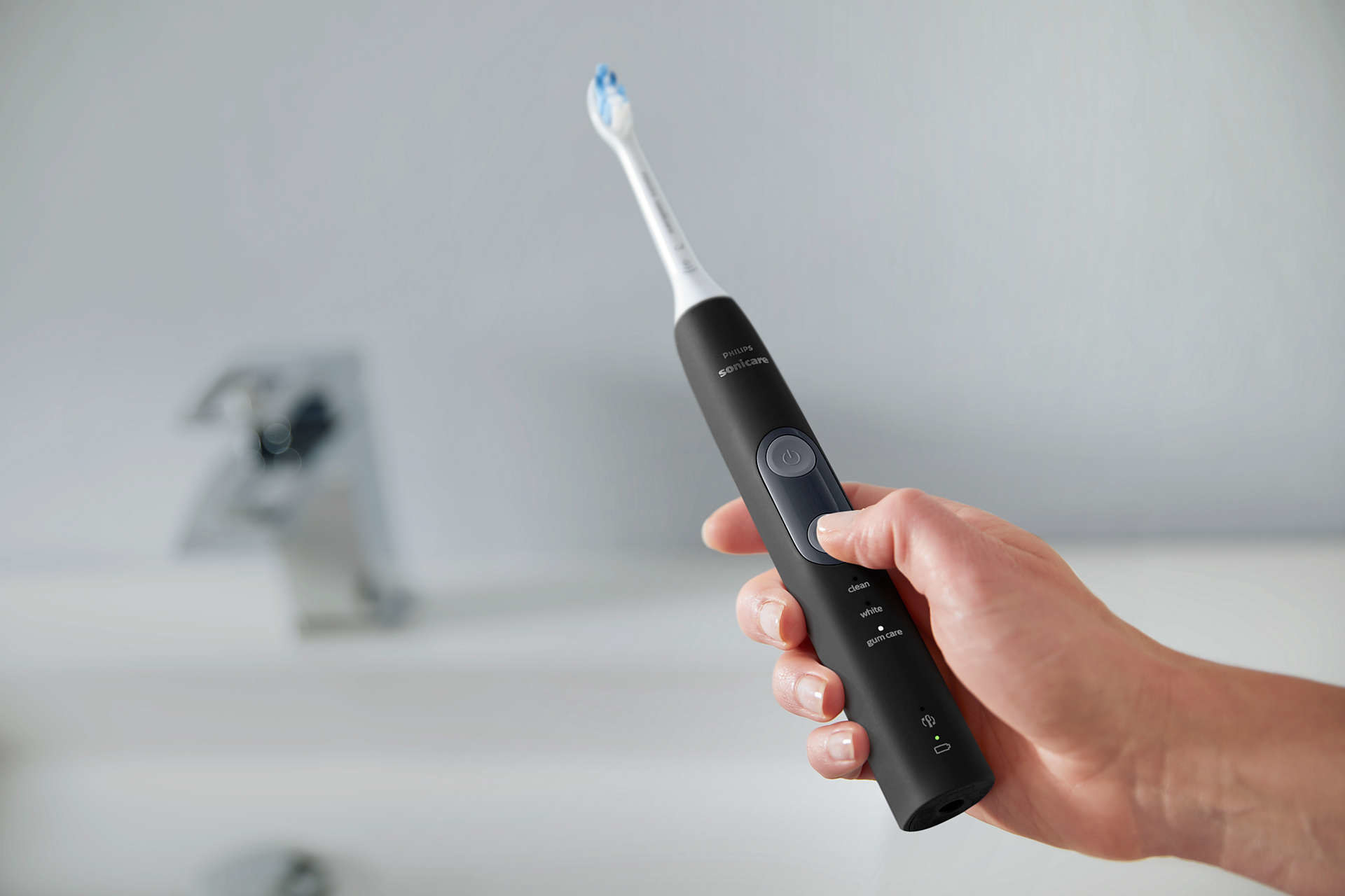 Hand holding an electric toothbrush with a black handle over a sink