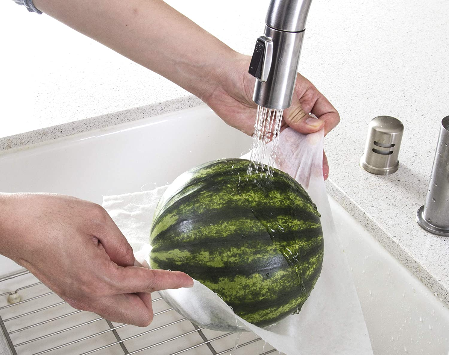 A person using a sheet from the package to hold a watermelon under a faucet