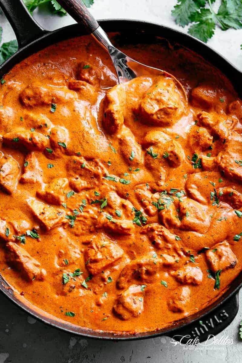 A cast-iron skillet with pieces of chicken in a creamy curry sauce.
