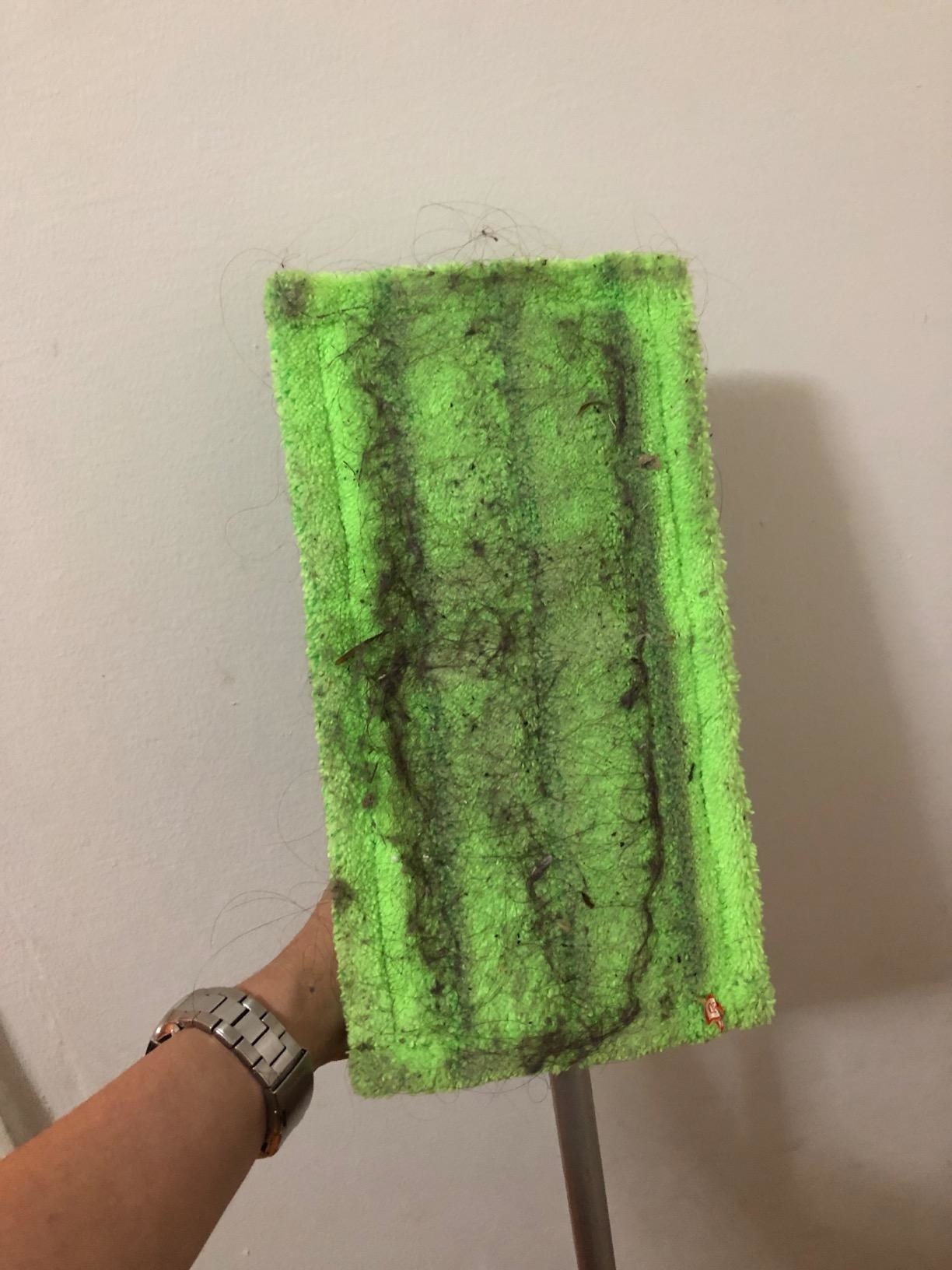 A reviewer showing the underside of her sweeper with the reusable pad having accumulated dirt and dust