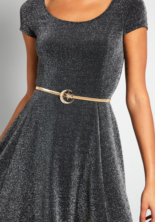 a model wearing the thin gold belt with a crescent moon and star buckle in the middle over a sparkly dress