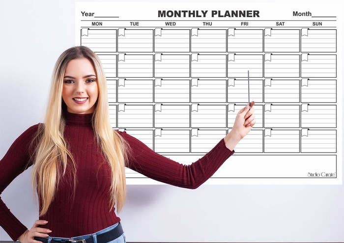A person pointing to the monthly planner hung on a white wall