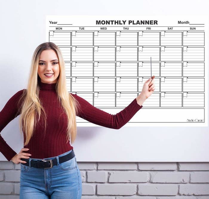 A woman pointing to the monthly planner hung on a white wall