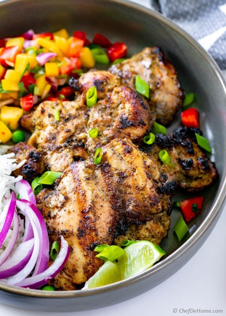 A bowl of jerk chicken with white rice, mango salsa, red onions, and limes.