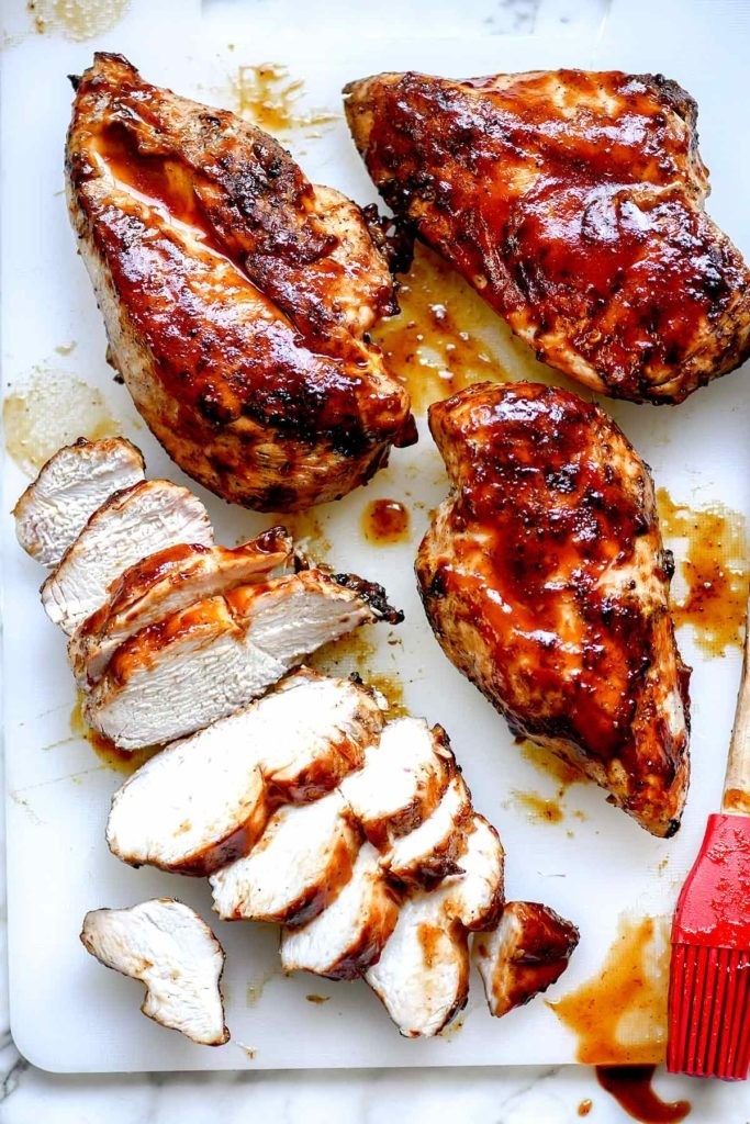 A few barbecue chicken breasts with some cut into slices.