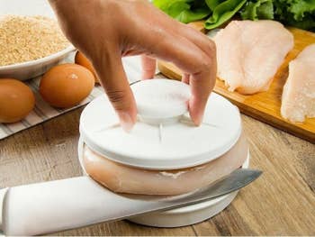 The two-piece kitchen slicer with a model's hand holding the handle on the top with a chicken breast being sliced in the middle