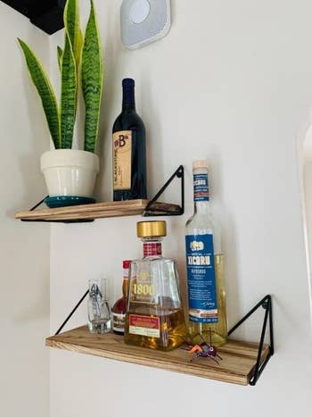 Reviewer's picture of the wooden floating shelves to display decorative bottles and plants