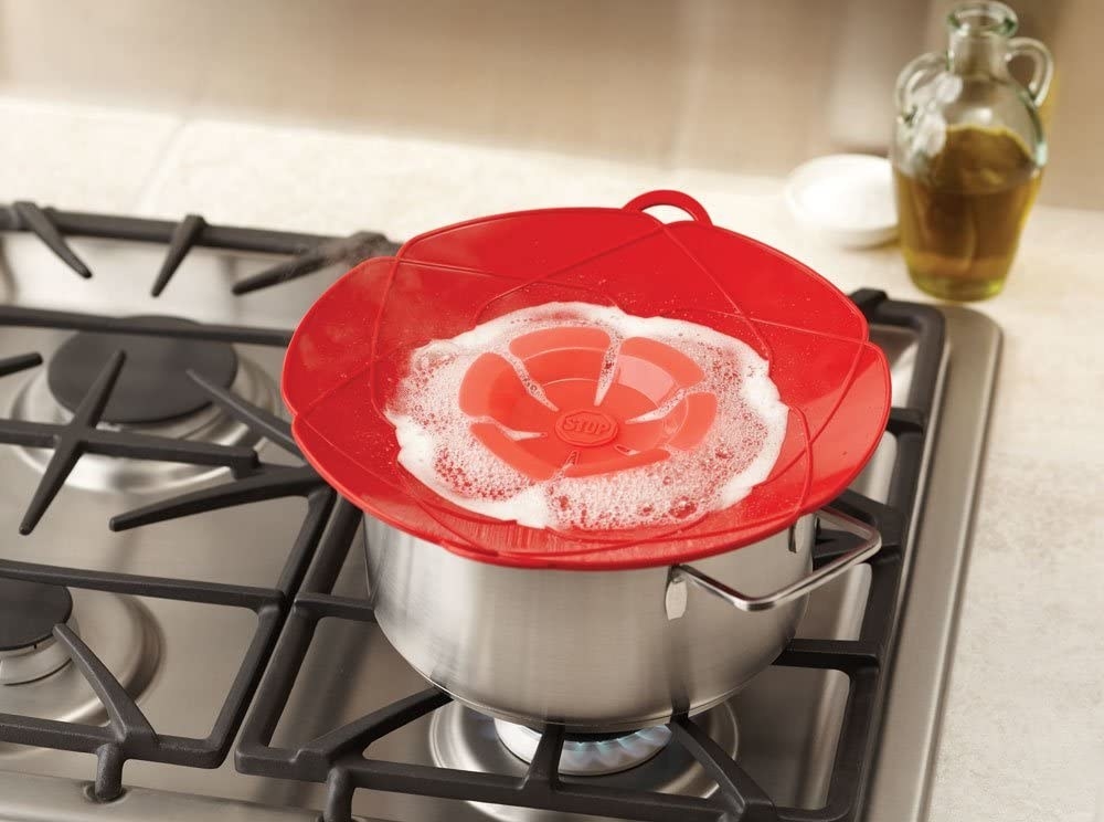 The spill stopper in red on top of a pot on a stove with water boiling inside, illustrating that it will not boil over