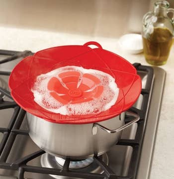 The spill stopper in red on top of a pot on a stove with water boiling inside, illustrating that it will not boil over