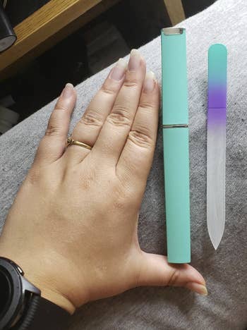 A reviewer's hand showing off their nails (which extend past their fingertips) beside a teal and purple version of the glass file