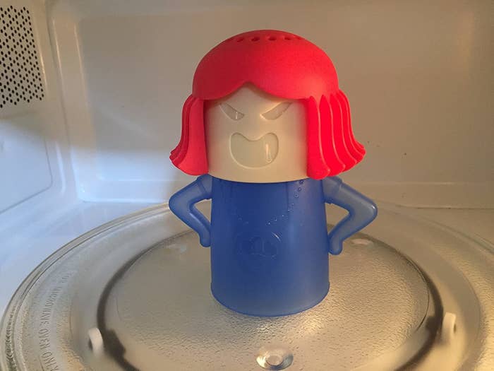 A plastic person with perforated holes on the top of their head sitting in a microwave